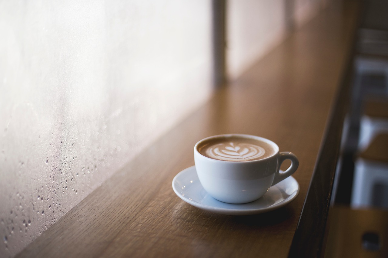 A latte with leaf art in a white cup and saucer on a wooden window counter